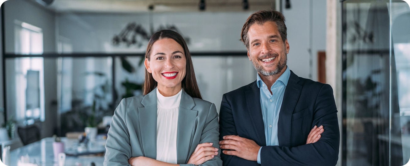 Dos ejecutivos, una mujer y un hombre de traje viendo a la cámara y sonriendo